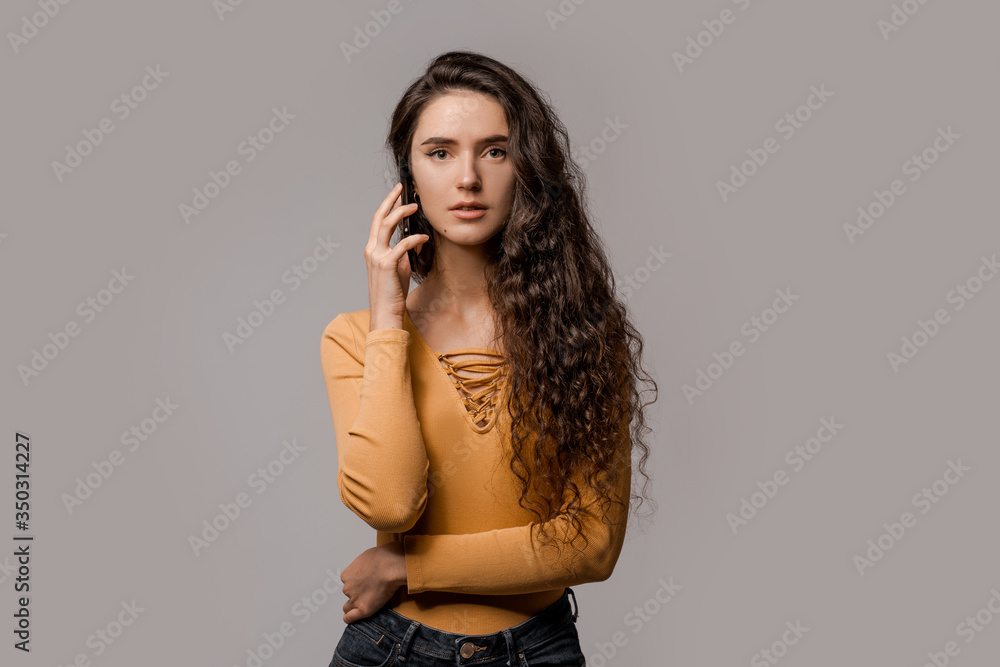 Chatting on mobile cell phone, online internet technology concept. 5g connecting and communication. Curly cute concentrated woman have a call dressed in yellow over grey background Chatting on mobile cell phone, online internet technology concept. 5g connecting and communication. Curly cute concentrated woman have a call dressed in yellow over grey background