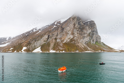 Maneuvering orange lifeboat in water in Arctic waters, Svalbard. Abandon ship drill. Lifeboat training. Man over board drill.