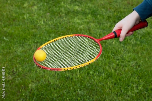 Badminton game with a ball on the nature. Child holds racket with ball on green grass background