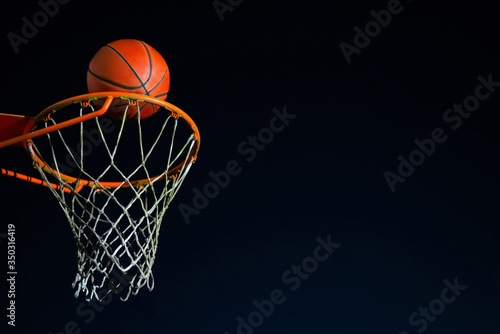 Street basketball ball falling into the hoop at night. Urban youth game. Close up of orange ball above the hoop net. Concept of success, scoring points and winning © CrispyMedia