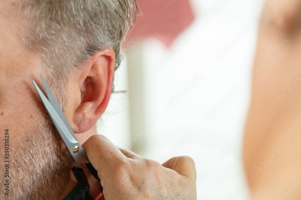 Fototapeta premium Home hairdresser cutting mans hair at indoors. Wife cutting husbands hair during quarantine.