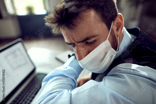 Businessman with face mask sneezing into elbow in the office.