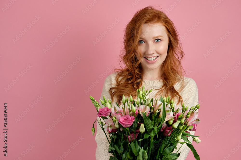 Cute red-haired girl with blue eyes smiles into a frame while standing on a pink background with a bouquet. Cute red-haired girl with blue eyes smiles into a frame while standing on a pink background with a bouquet.