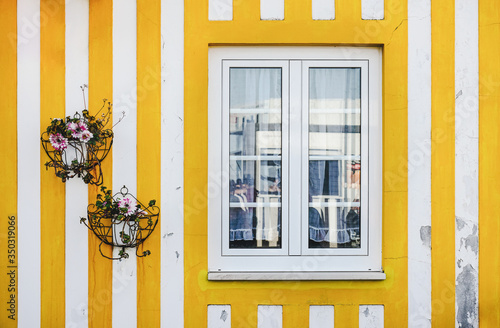 Vivid yellow and white wall of a traditional Costa Nova house with a window and two suspended flower beds.