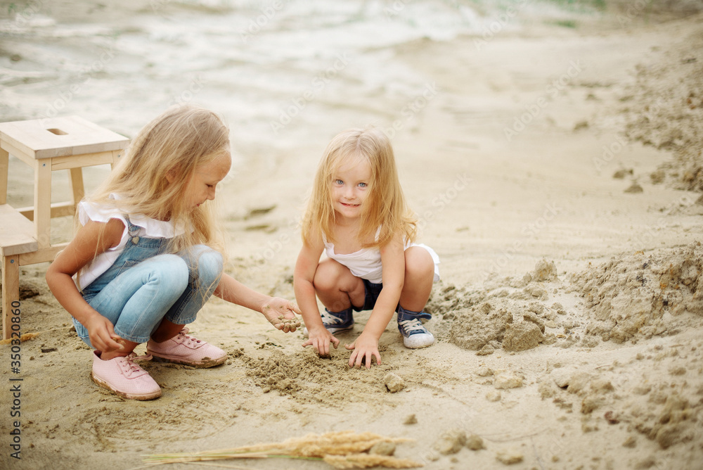 Cute sisters 7 and 3 years old play on a sandy beach in summer Cute sisters 7 and 3 years old play on a sandy beach in summer