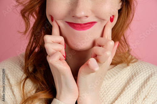 A close frame of women's lips with red lipstick and manicure, fingers pulls a smile.