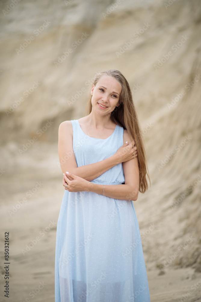 Beautiful young blonde with long hair walks along the sandy beach in a long light dress Beautiful young blonde with long hair walks along the sandy beach in a long light dress