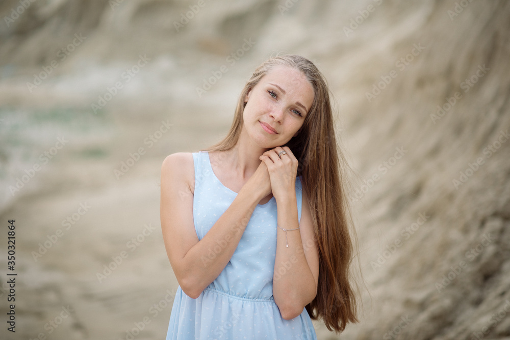 Beautiful young blonde with long hair walks along the sandy beach in a long light dress Beautiful young blonde with long hair walks along the sandy beach in a long light dress