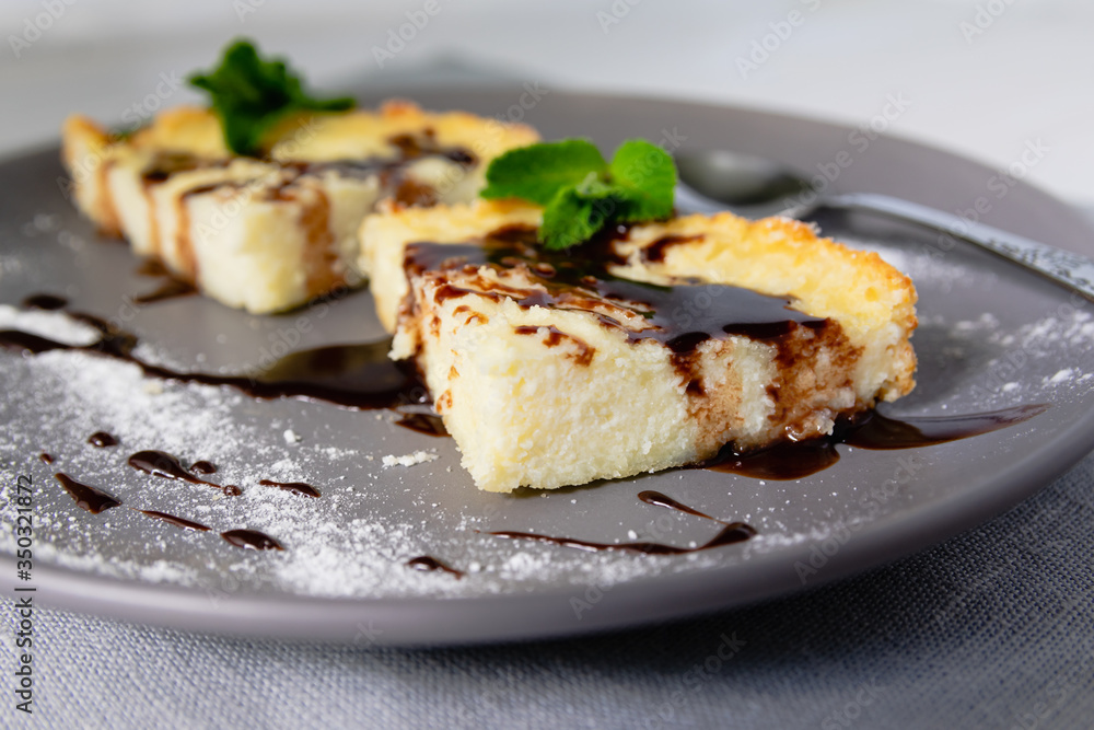 A serving of cheesecake in the form of triangular slices lies on a plate and is decorated with liquid chocolate closeup.