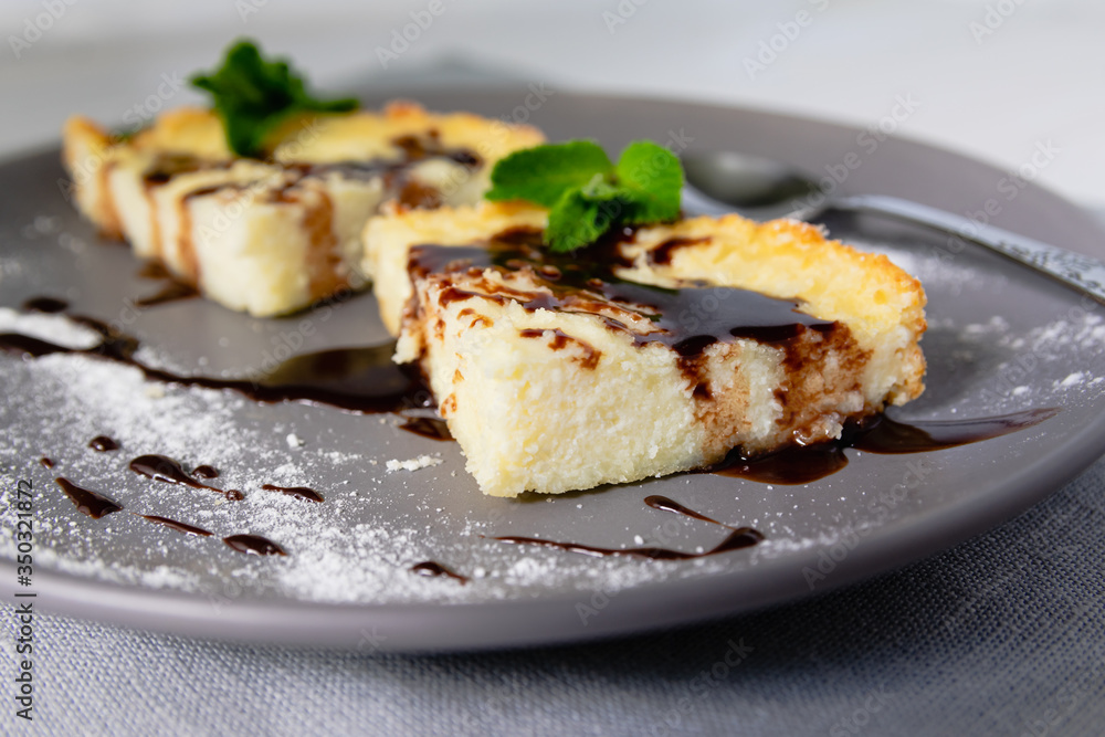 A serving of cheesecake in the form of triangular slices lies on a plate and is decorated with liquid chocolate closeup. A serving of cheesecake in the form of triangular slices lies on a plate and is decorated with liquid chocolate closeup.