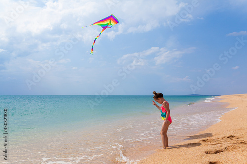 Child playing with a kite while running along the beach, in a summer sunny day. Have fun with your family during the holidays. Happy little girl launches a kite, summer vacation