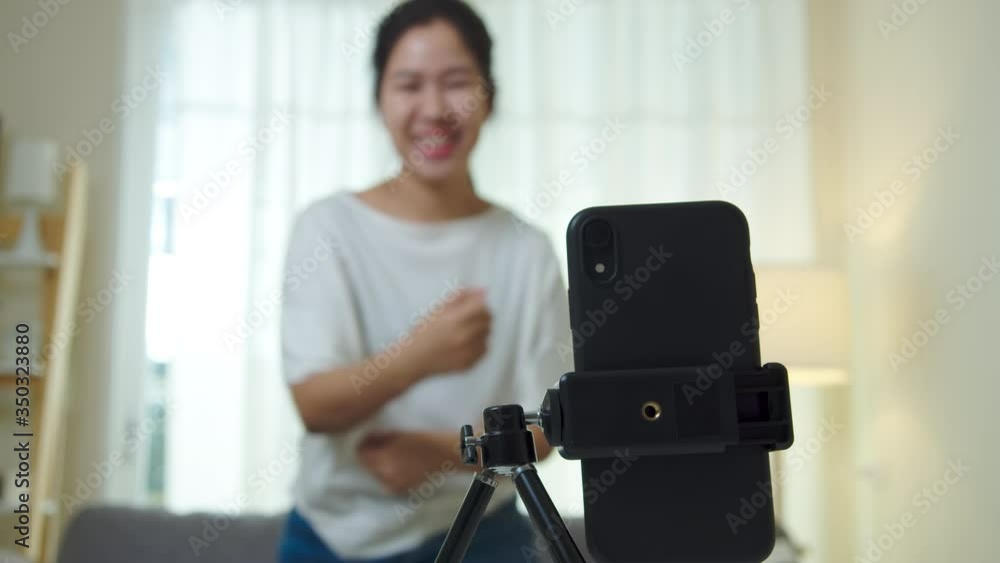 Asian woman creating short video by mobile application online service. Cute girl happy, enjoy and dance for sharing content to social media.Home entertainment online during quarantine from coronavirus Asian woman creating short video by mobile application online service. Cute girl happy, enjoy and dance for sharing content to social media.Home entertainment online during quarantine from coronavirus