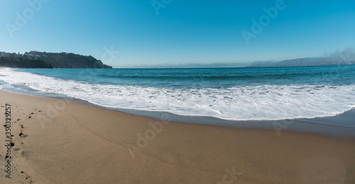 Gorgeous very beautiful panorama scenery of the ocean coast with blue water and clear light sand. Footprints in the sand. The houses stand on a hill in the background. No people. Sunny clear day
