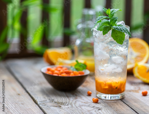 Sea buckthorn ice lemonade with oranges. Fruits and berries outdoors on a wooden table. Detox drinks.