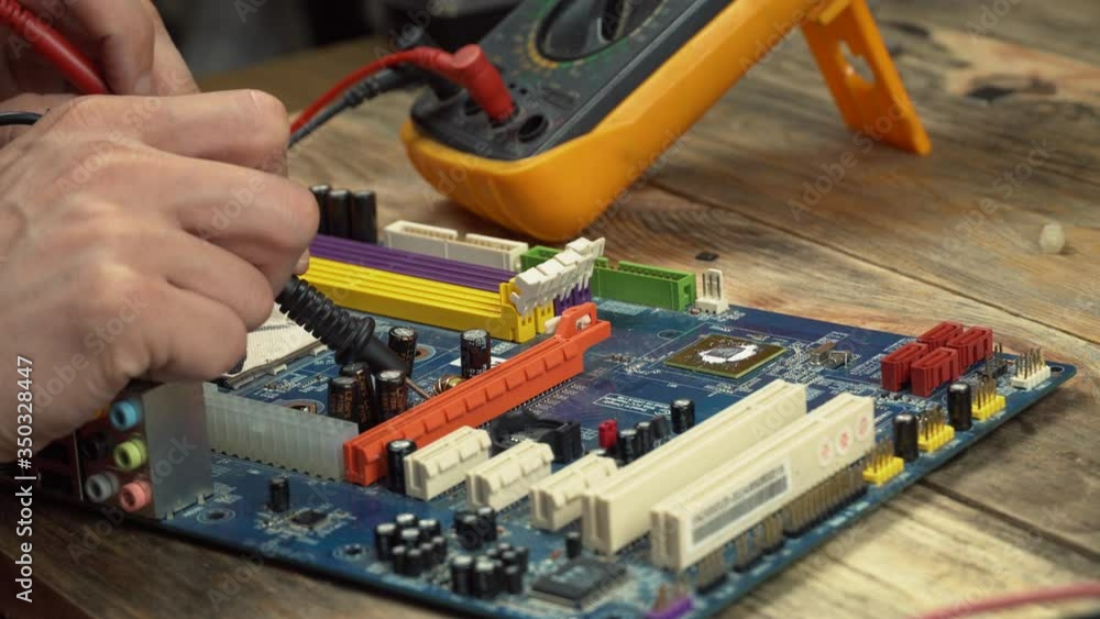 An engineer repairs a motherboard, he measures data with a multimeter. An engineer repairs a motherboard, he measures data with a multimeter.