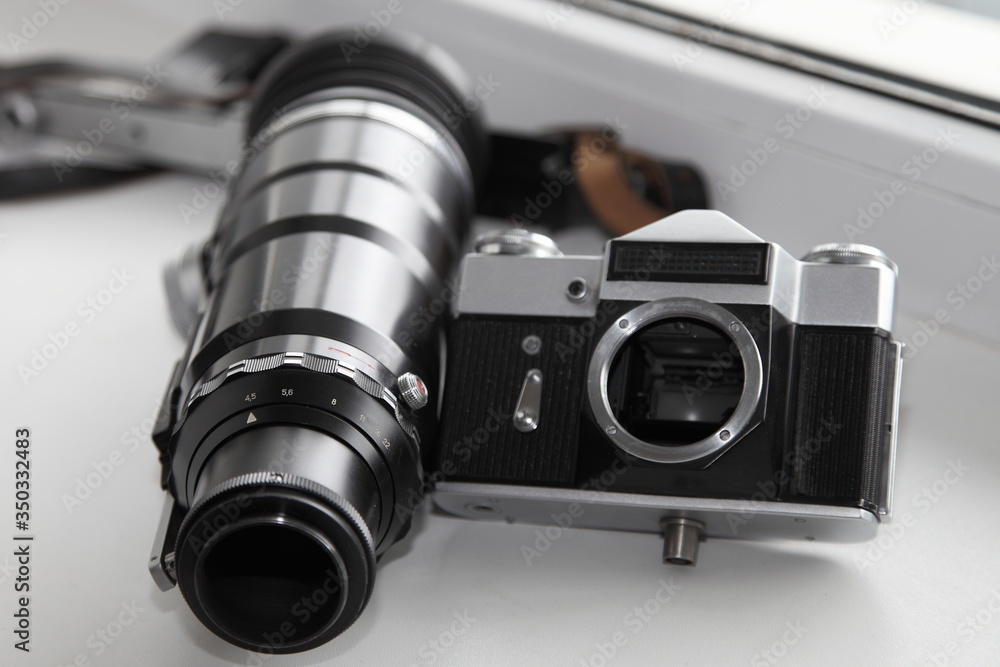 Manual aperture drive ring on professional metal vintage big telephoto lens near retro SLR film camera on white background