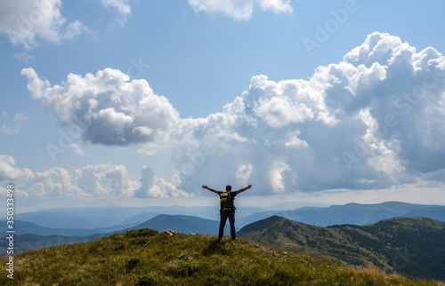 Young man with backpack standing with raised hands on peak of mountain and enjoying view. Sport and active life concept. Emotional scene.