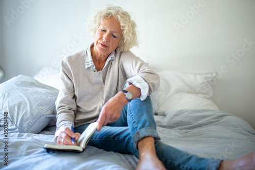 older woman sitting on bed writing in diary