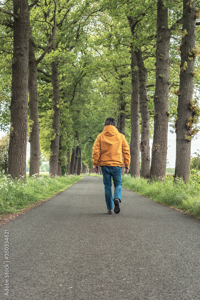 Man in yellow jacket and jeans walks on country road in springtime. Man in yellow jacket and jeans walks on country road in springtime.