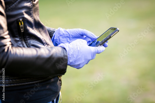 A woman in a black leather jacket and purple latex protective gloves holds a smartphone 