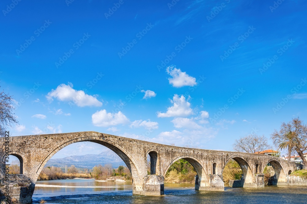 The famous old traditional stone bridge of Arta against a beautiful blue sky with clouds The famous old traditional stone bridge of Arta against a beautiful blue sky with clouds