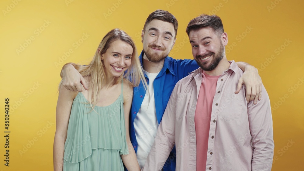 Happy fun guy appeares behind backs of his friends posing isolated on background. Family hipster portrait of three best friends laughing together at camera. Happy fun guy appeares behind backs of his friends posing isolated on background. Family hipster portrait of three best friends laughing together at camera.