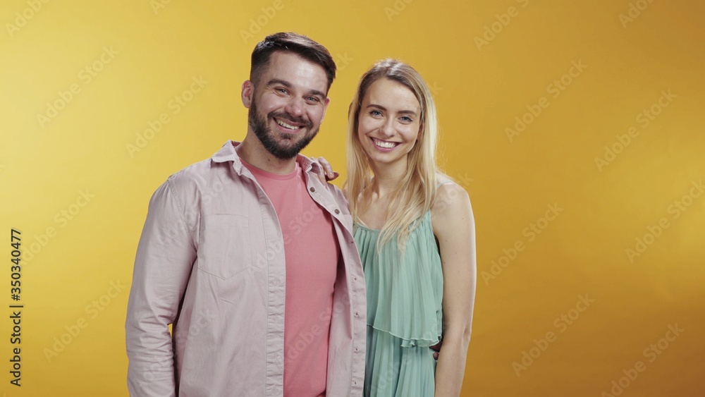 Fototapeta premium Cute caucasian young couple standing and posing on orange background. Their funny bearded friends appearing behind backs smiling happy together. Copy space. Friendship.