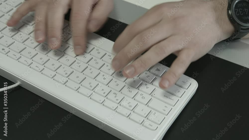 Man sitting in a modern office typing on a white computer keyboard Man sitting in a modern office typing on a white computer keyboard