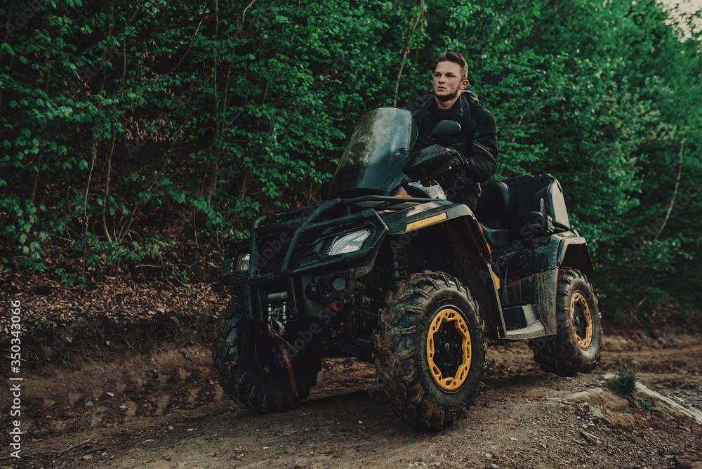 Fototapeta premium A young man in a white helmet rides through the woods on a Quad bike. Extreme hobby. A trip to ATV on the road from logs. Quad Biking through the forest.