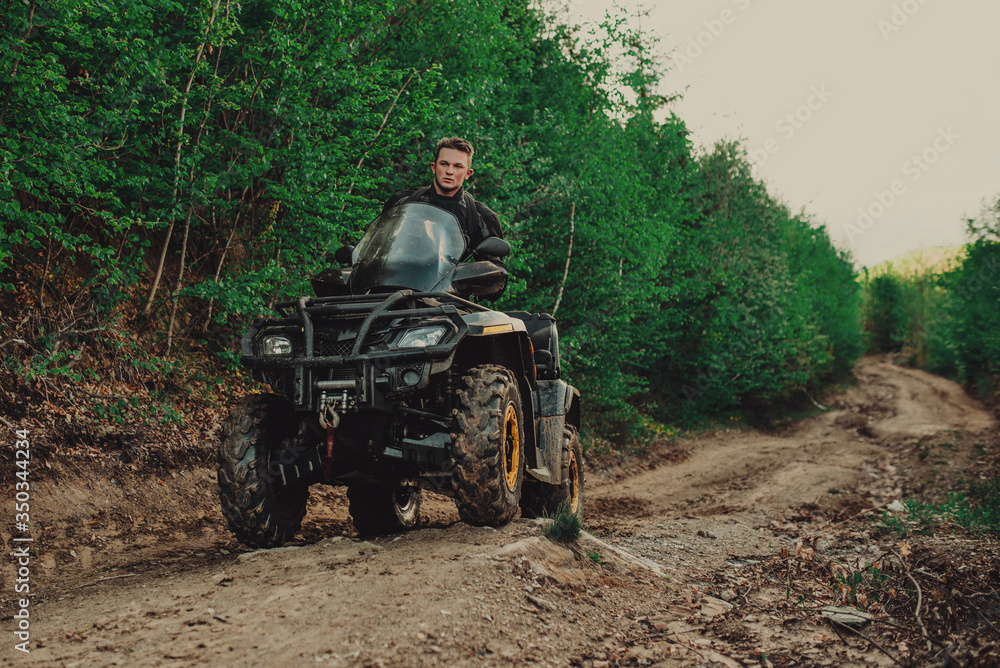 A young man in a white helmet rides through the woods on a Quad bike. Extreme hobby. A trip to ATV on the road from logs. Quad Biking through the forest. A young man in a white helmet rides through the woods on a Quad bike. Extreme hobby. A trip to ATV on the road from logs. Quad Biking through the forest.