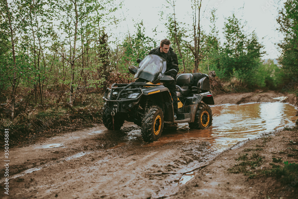 Fototapeta premium A young man in a white helmet rides through the woods on a Quad bike. Extreme hobby. A trip to ATV on the road from logs. Quad Biking through the forest.