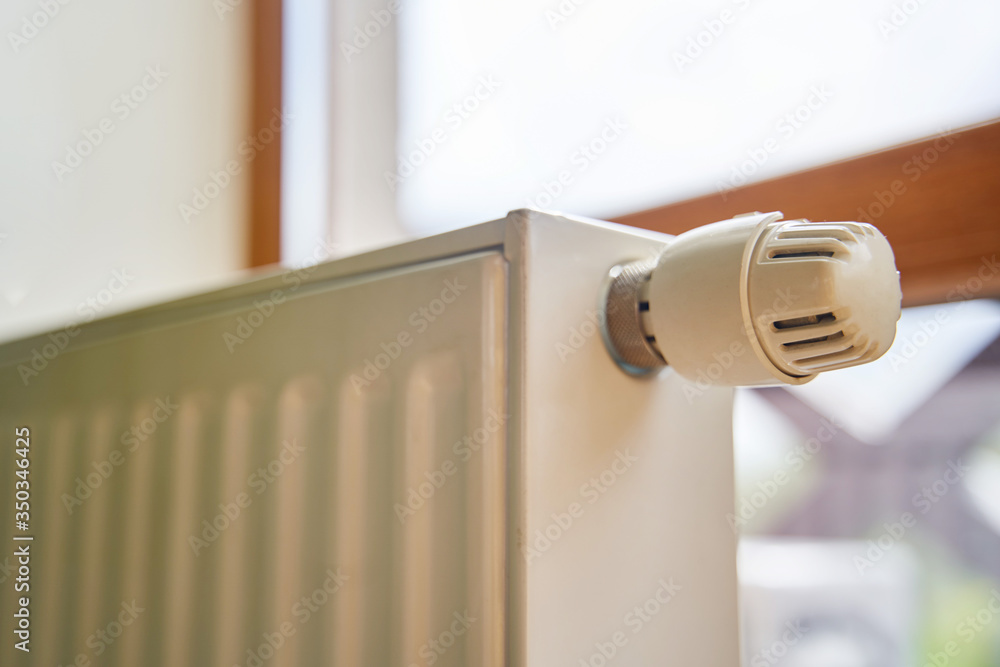 Radiator in the apartment. White heated battery. Thermostat head of a heating radiator in an apartment, office. Radiator in the apartment. White heated battery. Thermostat head of a heating radiator in an apartment, office.
