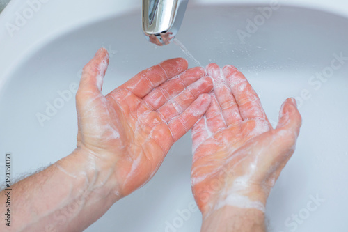 Man washing hands with soap under bathroom sink.