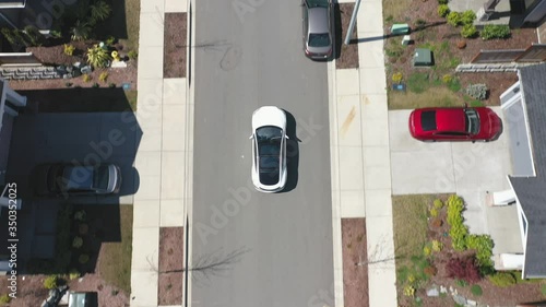 Aerial view of a white car driving through a suburban neighborhood arriving at home; drone follow shot