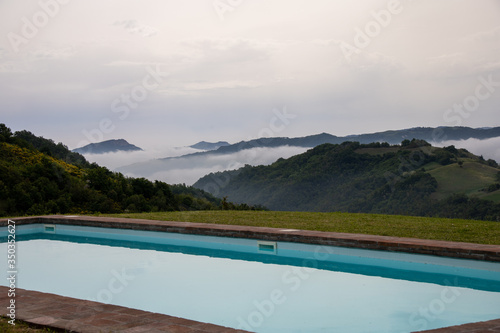 Wide angle view of a part of a private swimming pool in a countryside location. Low clouds lingering among the mountains in the background. Weather and luxury.