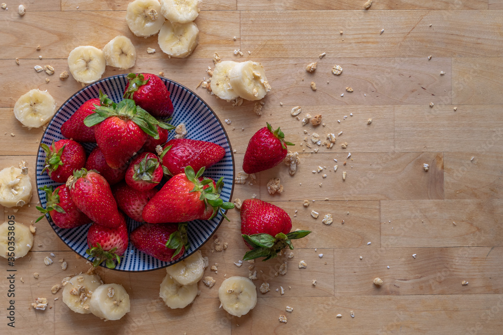 Top down image of Whole Strawberries on a Plate Surrounded by Granola and Banana Slices Top down image of Whole Strawberries on a Plate Surrounded by Granola and Banana Slices
