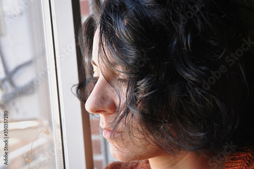 .Worried young woman looks out the window from her home. Isolation concept.