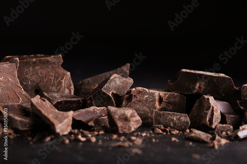Pieces of dark chocolate on black table, closeup