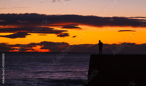 Fisherman silhouette on dock at sunset over sea
