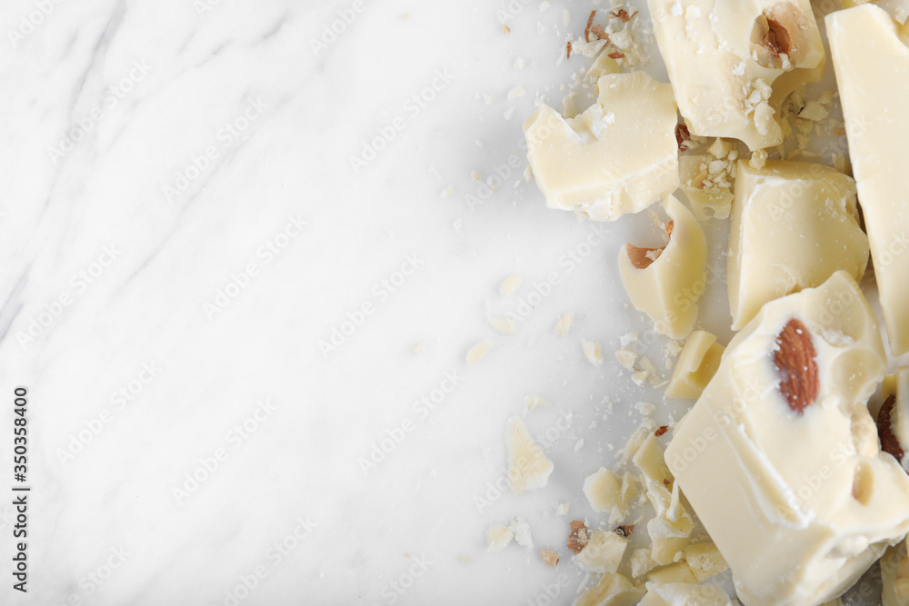 Pieces of white chocolate with nuts on marble table, flat lay. Space for text Pieces of white chocolate with nuts on marble table, flat lay. Space for text