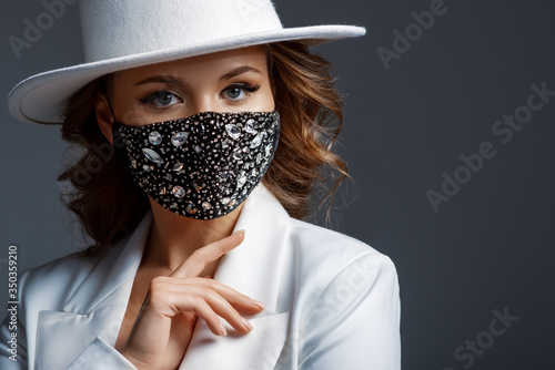 Elegant woman wearing trendy fashion outfit during quarantine of coronavirus outbreak. White suit including stylish luxury black face mask with rhinestones. Close up studio portrait. Copy, empty space photo