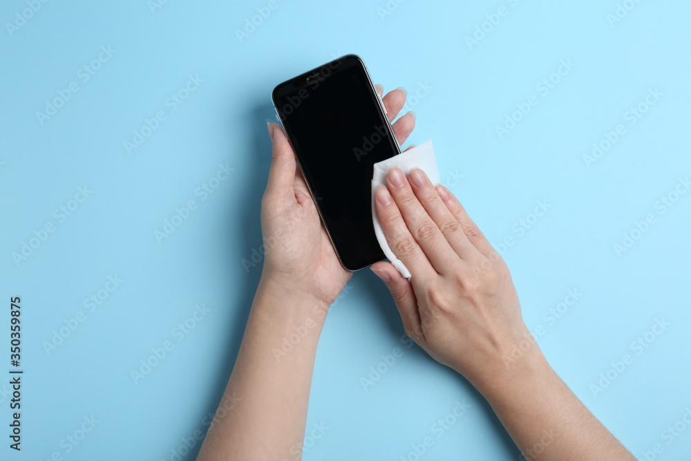 Woman cleaning mobile phone with antiseptic wipe on light blue background, top view Woman cleaning mobile phone with antiseptic wipe on light blue background, top view