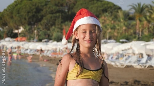 Little adorable girl in red Santa hat having fun at beach.