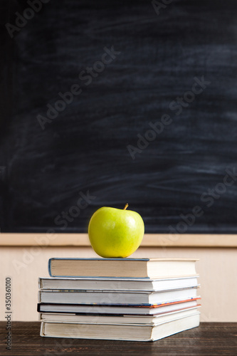 Books, apple, pens, pencils and glasses on a wooden table, against the background of a chalk board. Concept for Teacher's Day, copy space.