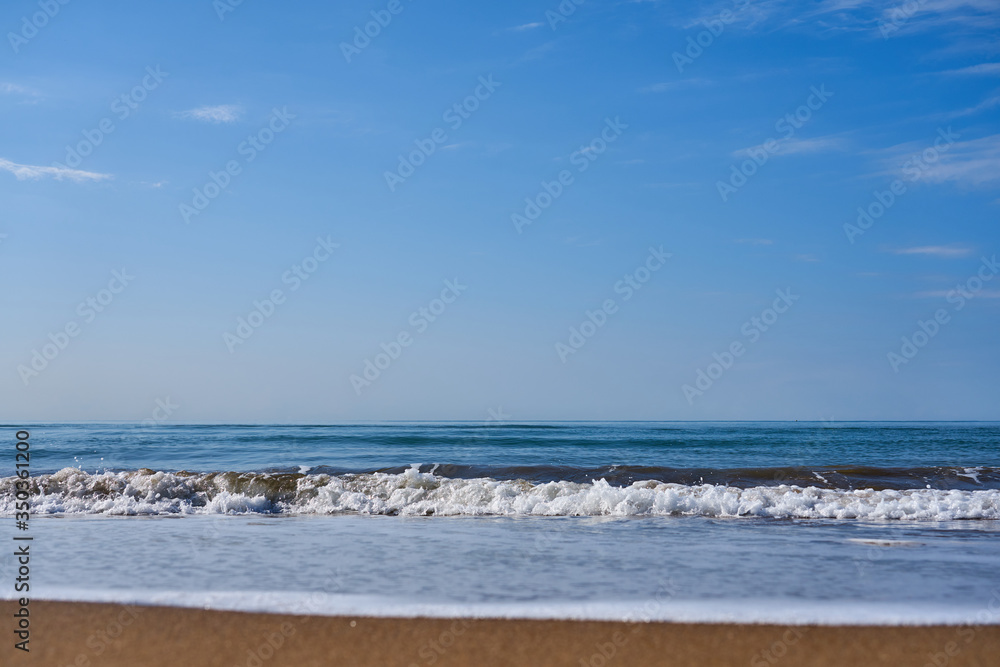 Blurred sea wave with foam on a sandy beach with horizont as a natural background/texture.