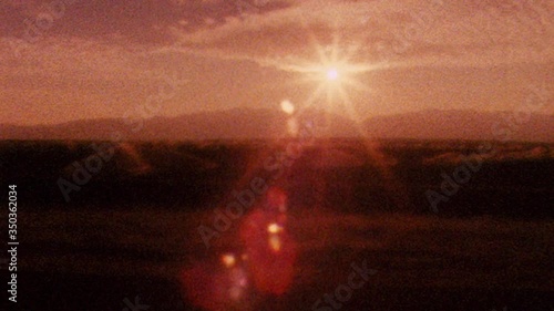 Shaky old looking archival footage drving on 101 highway towards Los Angeles past dessert as sun sets in the distance. Film texture, grit, grain, dust and flash frames create historical look and feel