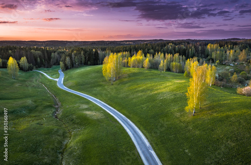Aerial landscape of countryside with colorful storm clouds. Warm sunset  over a pine forest and curvy road.