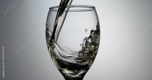 Closeup shot of glass being filled up with stream of alchoholic white wine in slow motion, pouring beverage into goblet, isolated on white background photo