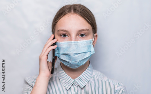 Close-up, teenager girl in medical mask, calls her parents on smartphone, listens voice message, looks at camera. Emotions anxiety worries for loved ones call from hospital. White background.