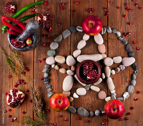 Pentagram made of stones with pomegranate, apples and red hot chili peppers on a wooden background.